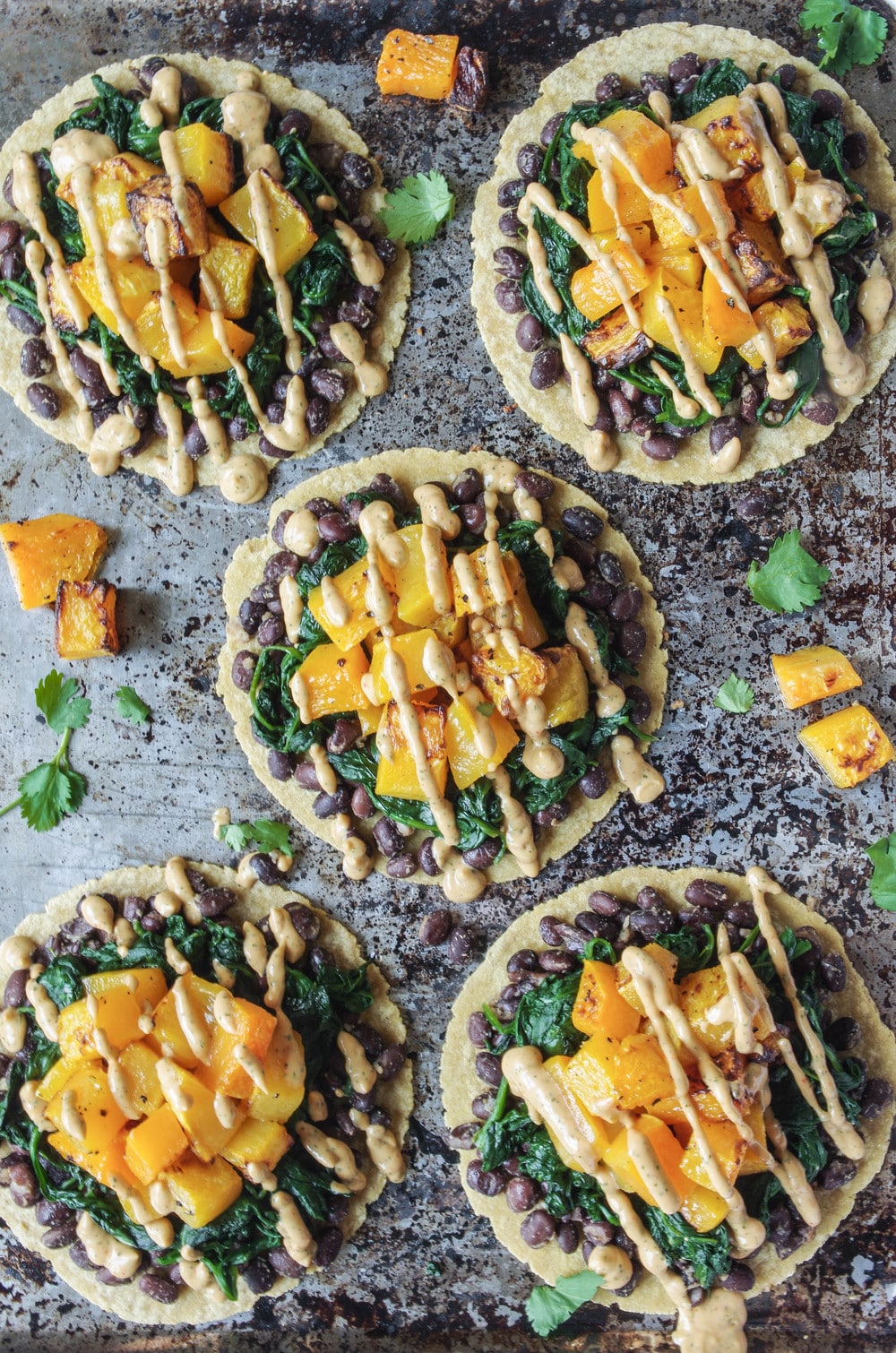 Overhead image of 5 tortillas with black beans, cooked spinach, roasted butternut squash, and chipotle lime crema