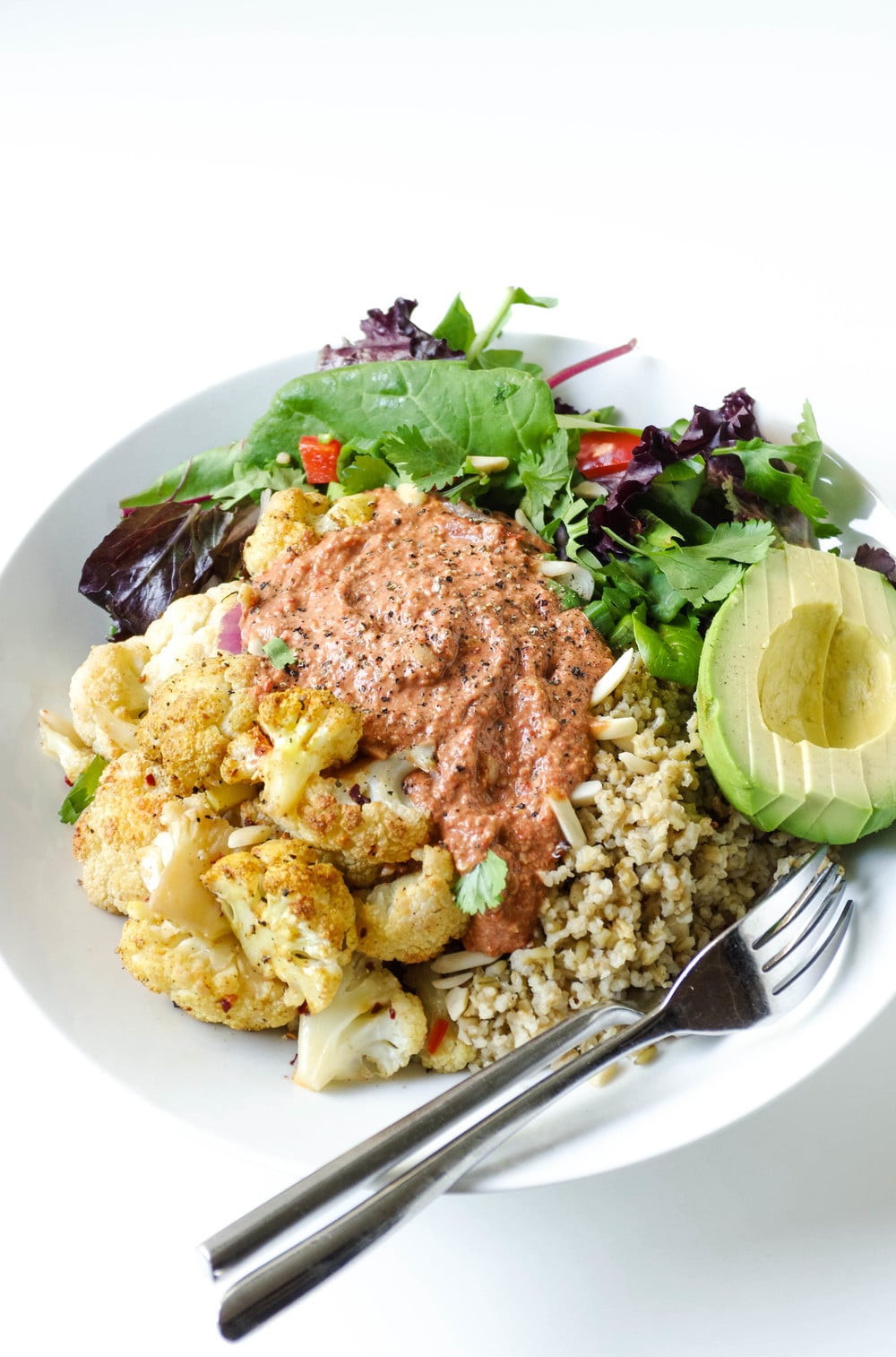 close up of Freekeh Salad in a white Bowl with Roasted Red Pepper, Walnut + Tahini Sauce