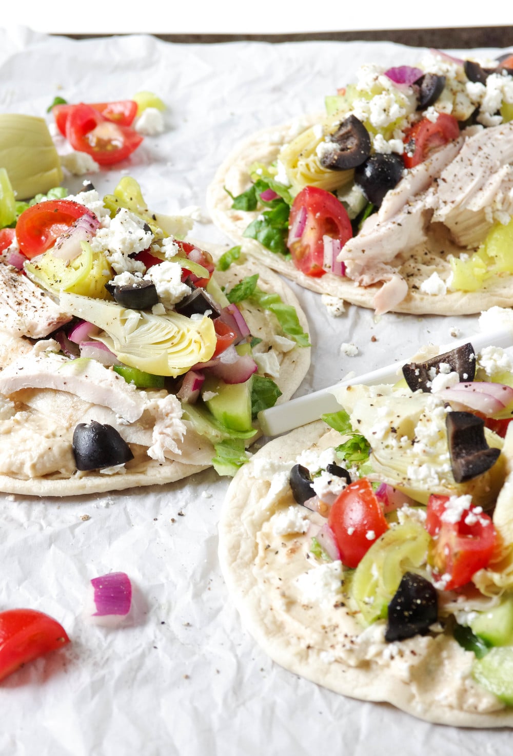 Three Mediterranean Chicken Wraps made with hummus, salad, chicken and feta cheese on a baking sheet lined with parchment paper.