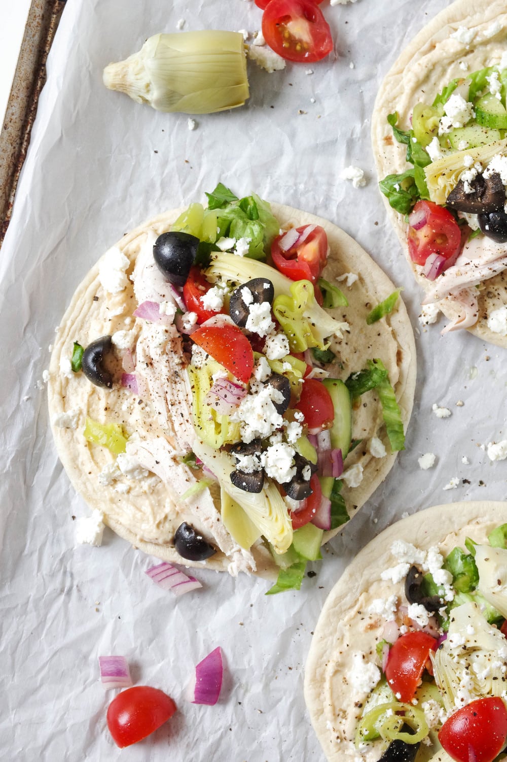 Three Mediterranean Chicken Wraps made with hummus, salad, chicken and feta cheese on a baking sheet lined with parchment paper.