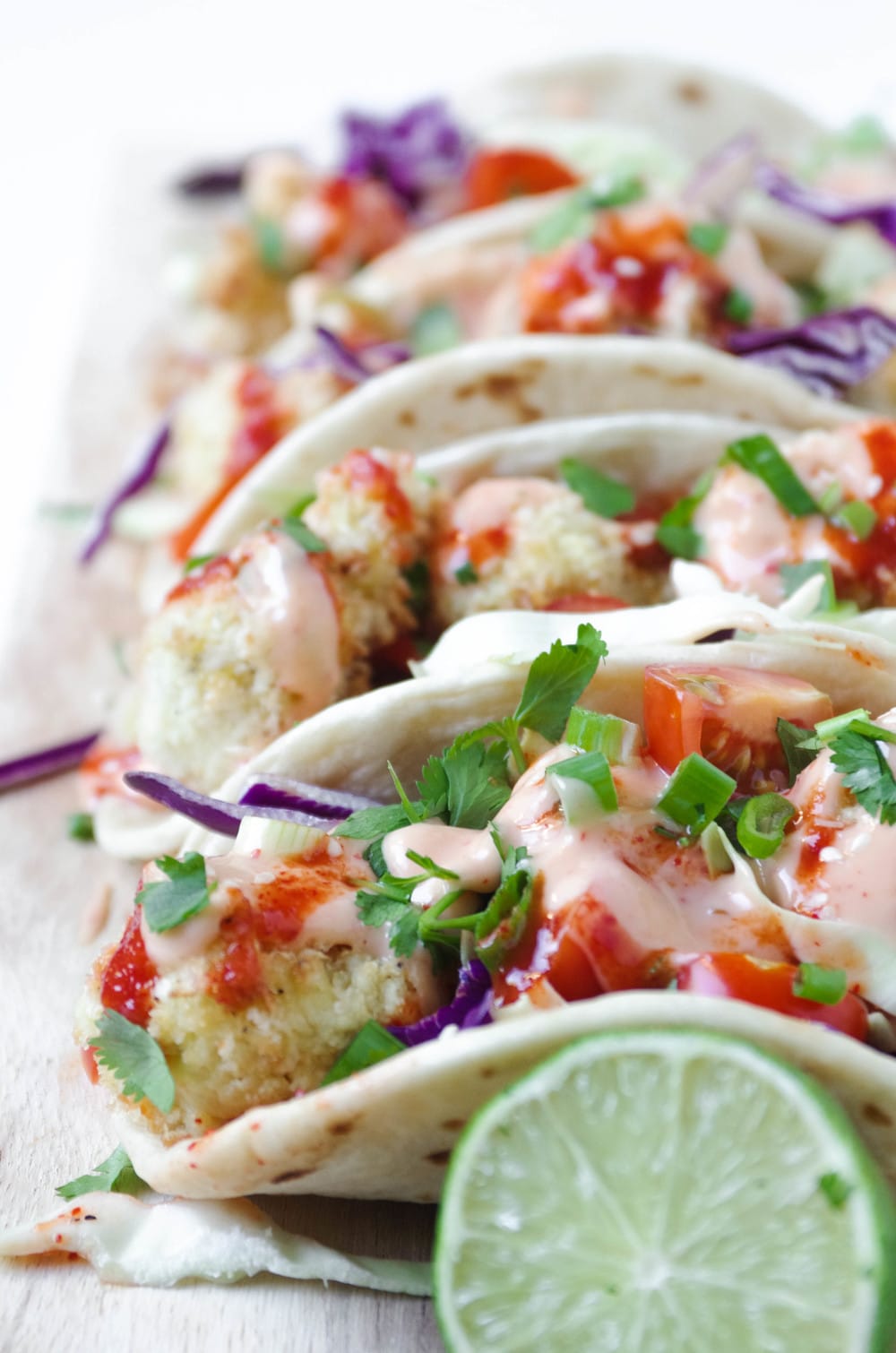 4 Cauliflower Tacos lined up on cutting board with lime