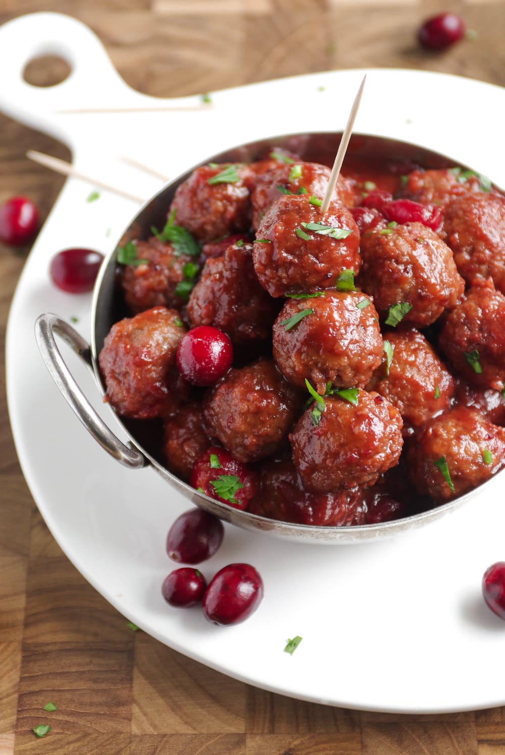 Silver bowl filled with party-size cranberry sauce covered meatballs garnished with fresh parsley.