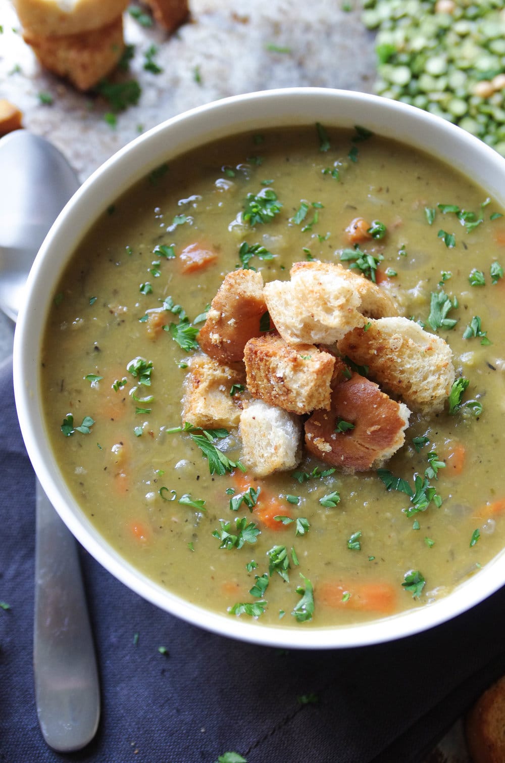 White bowl filled with split pea soup with ham and topped with croutons.